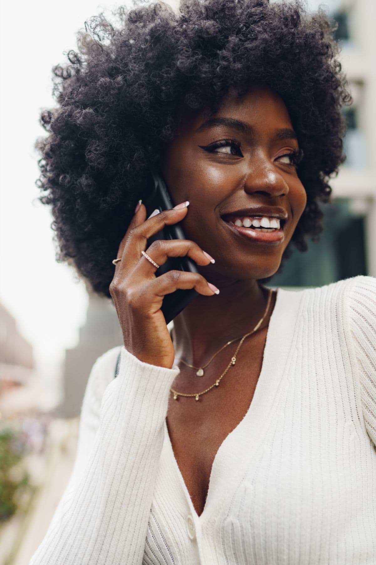 A woman smiling while talking on her phone outdoors.